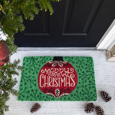 a christmas door mat with the words merry christmas written on it next to pine cones