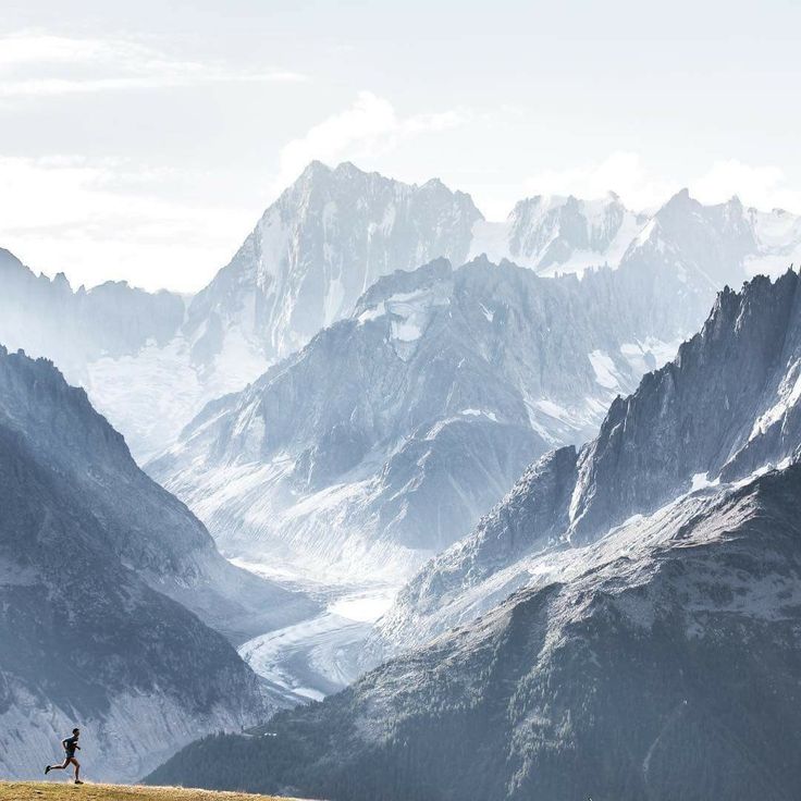 a person standing on top of a grass covered hill with mountains in the back ground