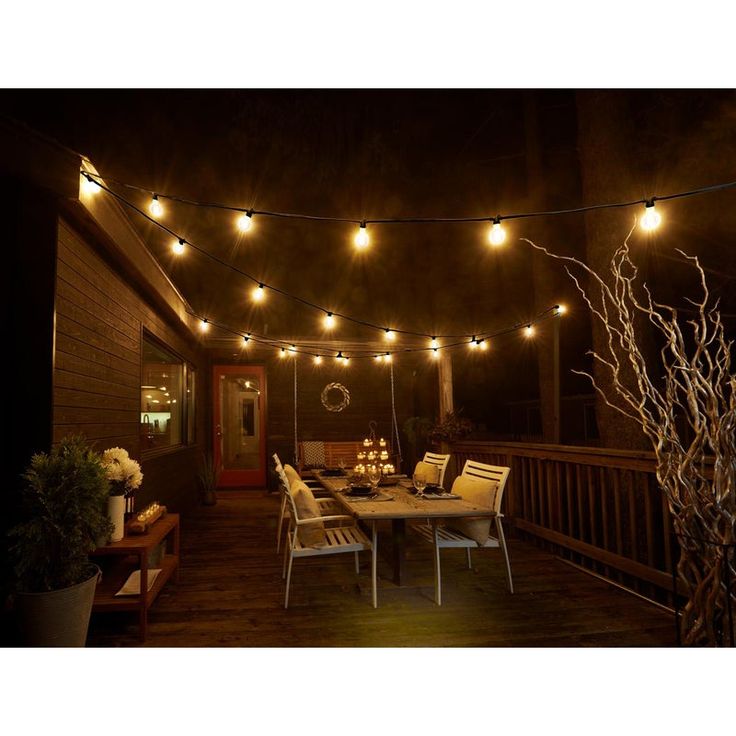 an outdoor patio with lights strung over the table and chairs on the deck, next to a potted plant