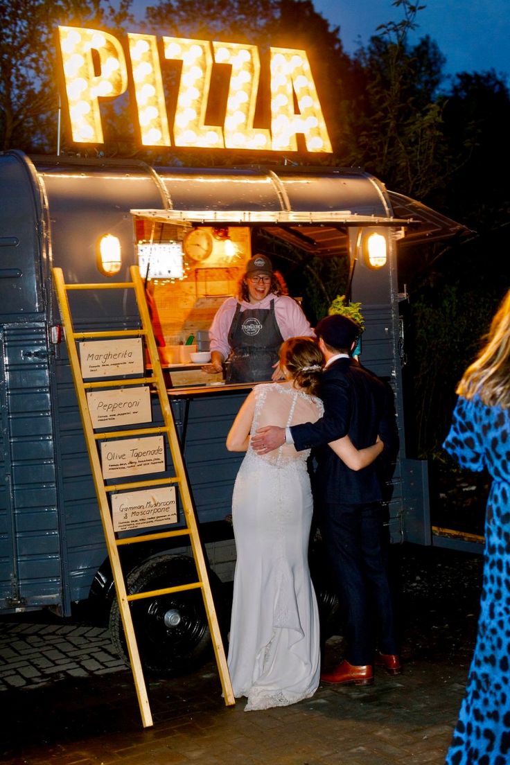 a man and woman standing in front of a food truck with the word pizza written on it