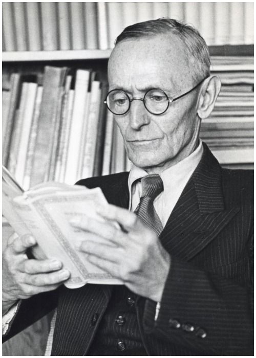 an older man sitting in front of a bookshelf reading a book while wearing glasses