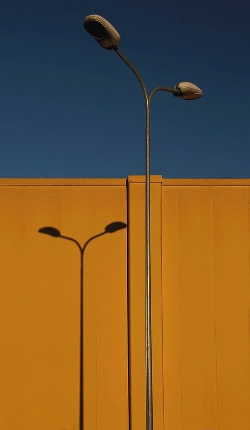 two street lamps are next to a yellow wall