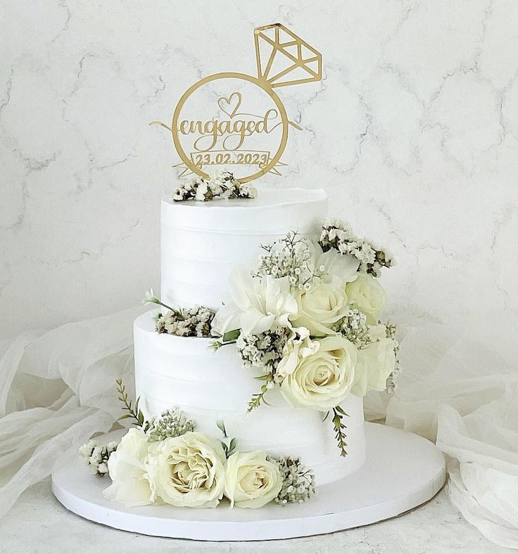 a wedding cake with white flowers and gold lettering on the top is sitting on a table