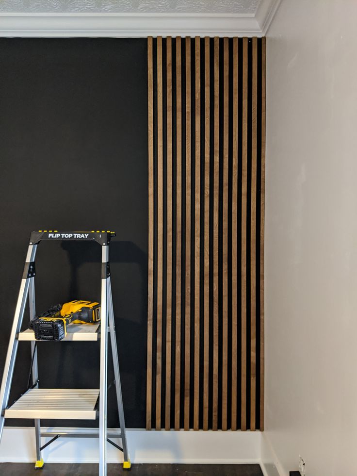 a ladder stands in front of a black wall with vertical striped drapes on it