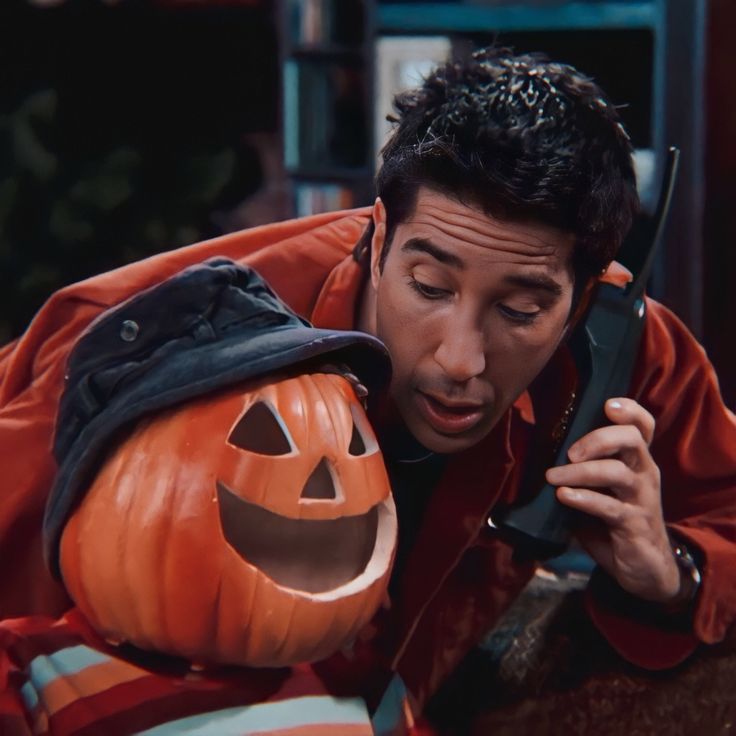 a man talking on a cell phone next to a carved pumpkin