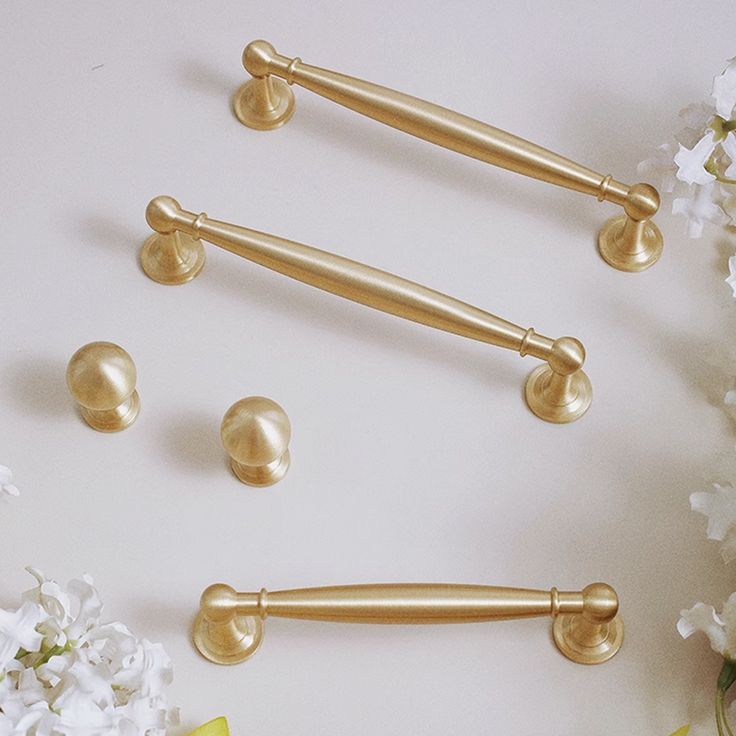 three gold handles and two knobs on a white surface with flowers in the background