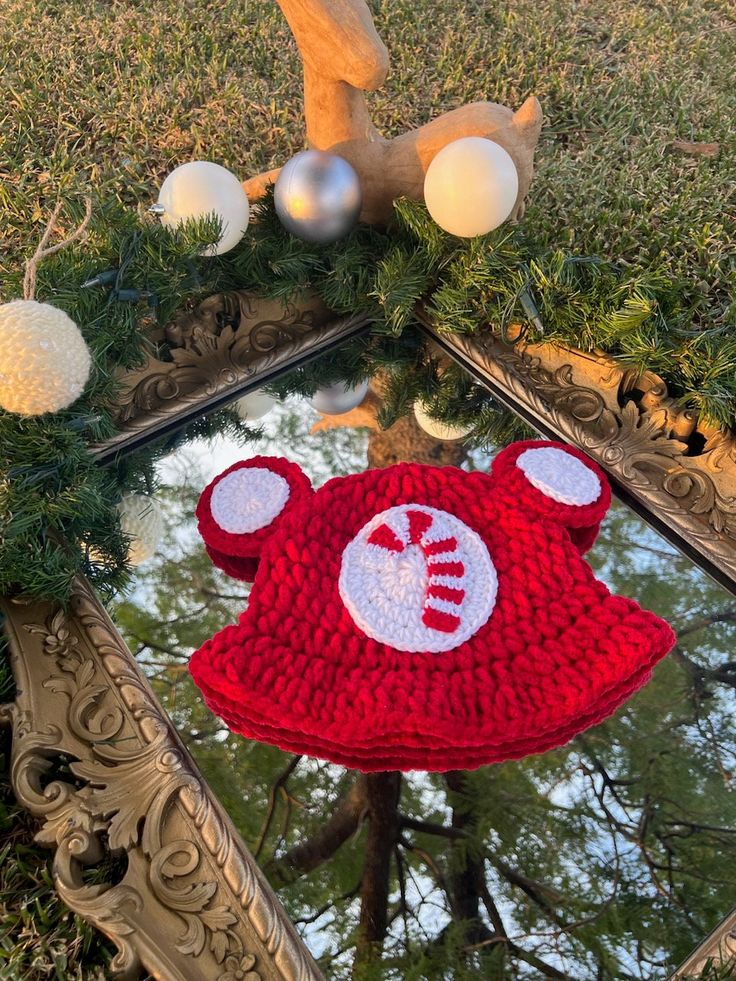 a knitted bear hat sitting on top of a mirror next to christmas ornaments and decorations