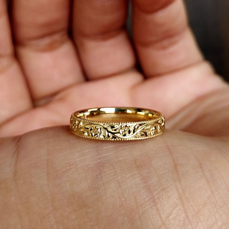 a close up of a person's hand holding a gold wedding ring with filigrees on it