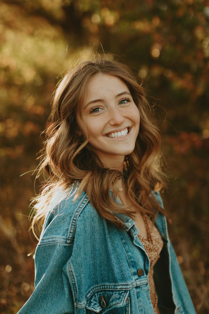 a smiling woman wearing a jean jacket in the woods