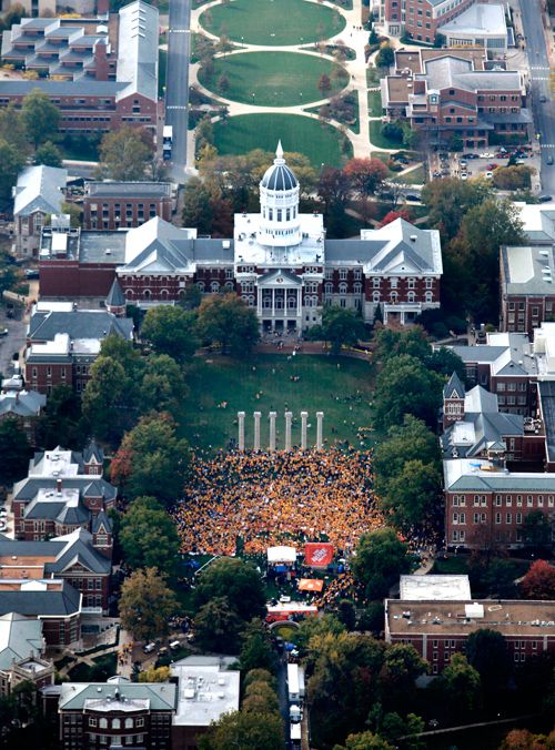 an aerial view of a large building with lots of people in the yard and trees surrounding it