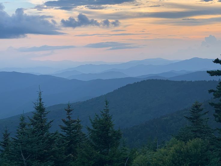 the mountains are covered in trees as the sun is setting over them and there is no image to provide a caption for