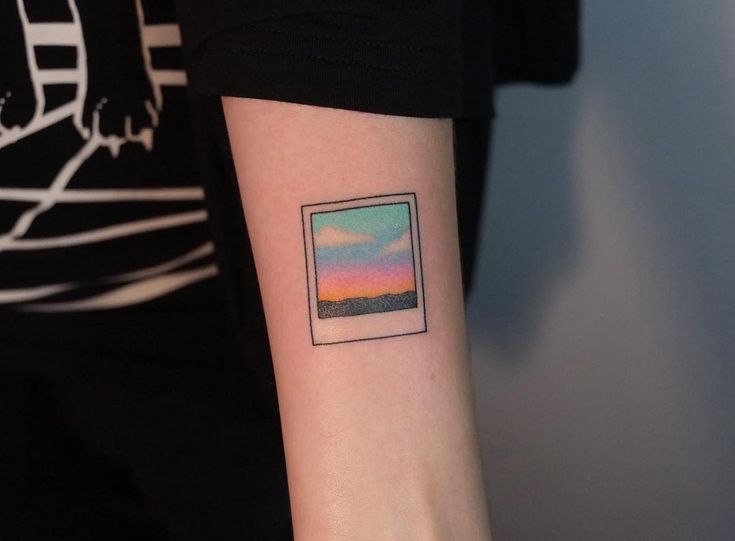 a person with a small square tattoo on their left arm and the sky in the background