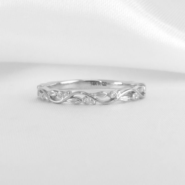 a white gold wedding band with leaves on the side and diamonds in the middle, sitting on top of a white cloth