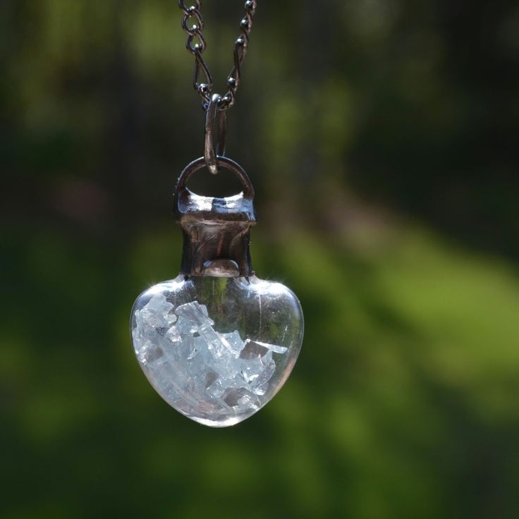 This shaker heart necklace for women is a unique piece of fidget jewelry that captivates with its Icy blue glass shards encased in a stunning glass heart pendant. The shards move freely within the pendant, offering a soothing and mesmerizing effect, perfect for those who enjoy tactile experiences. This exquisite necklace makes an ideal coworker promotion gift, combining elegance with a touch of playful charm. Icy blue glass shards fill this hand blown glass heart bottle. The blue glass moves freely inside making this pendant both eye catching as well as uniquely interesting. Hand formed and soldered bail and cap. The top is sealed and cannot be opened. Custom requests welcome.  * Pendant dimensions: 1 1/2"H x 1"W (38 x 25mm)  * Your choice of chain length, select at checkout. 22", 24" and Adjustable Glass Heart Pendant Jewelry, Glass Heart Pendant Necklace For Gift, Clear Glass Jewelry For Healing, Silver Glass Necklace Keepsake, Clear Glass Healing Jewelry, Silver Glass Necklace For Keepsake, Clear Heart Pendant Jewelry Gift, Clear Heart Pendant Jewelry As Gift, Glass Heart Beads Necklace As A Gift