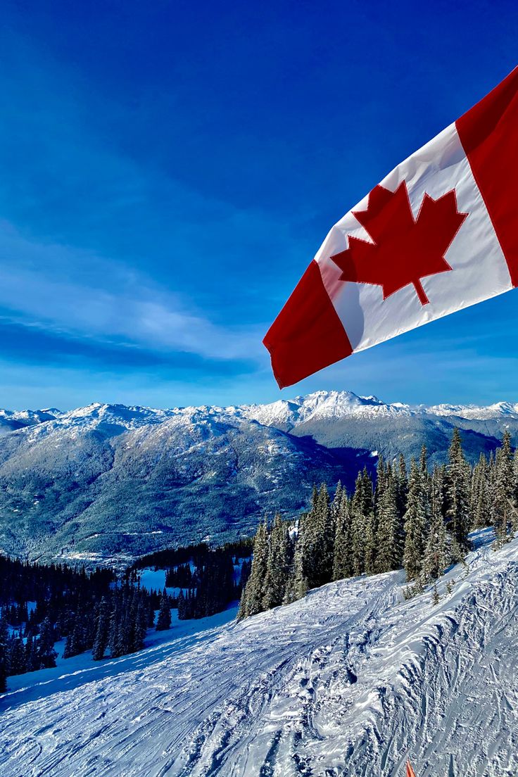 the canadian flag is flying high above the snow covered slopes in front of some mountains