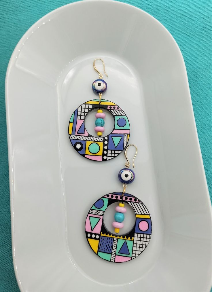 two colorful earrings are hanging from a white plate on a blue tablecloth with a turquoise background