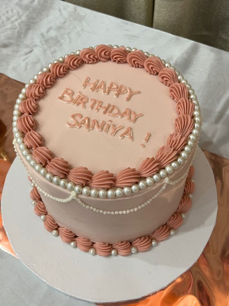 a birthday cake with pink icing and white frosting on top sitting on a table