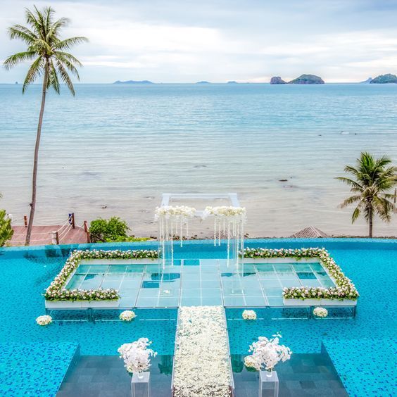 an outdoor wedding setup in the middle of a swimming pool with water and palm trees