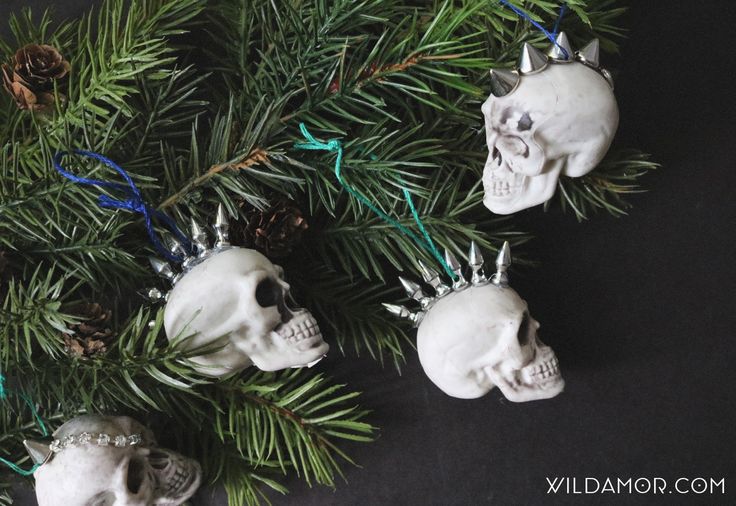 three skulls wearing crowns are hanging from the branches of a christmas tree in front of pine cones