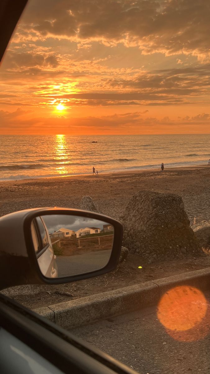 the sun is setting on the beach as seen through a car's side view mirror