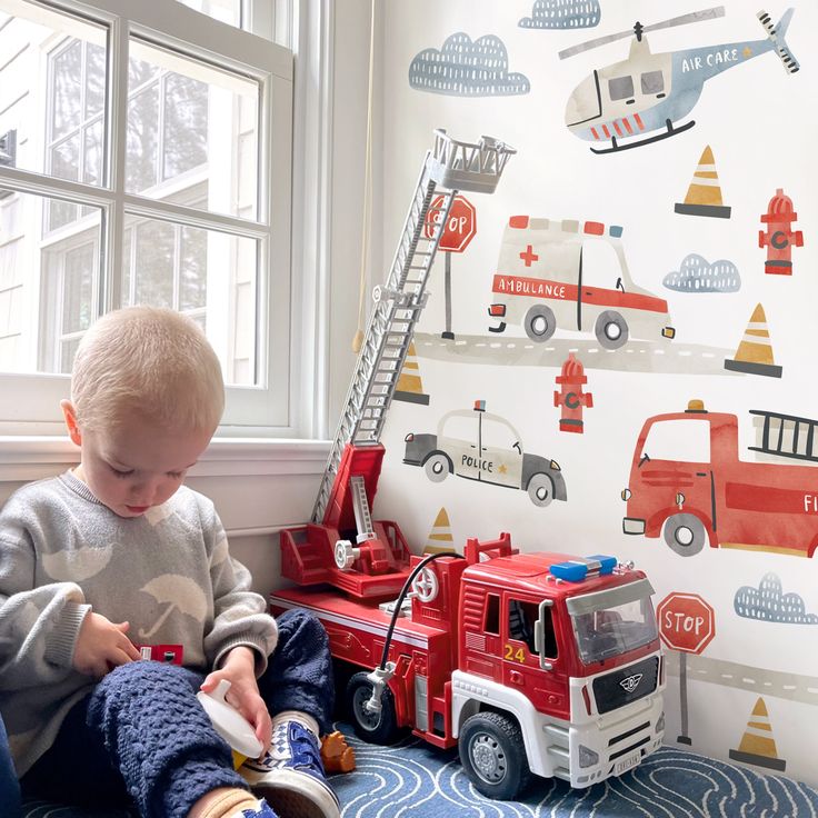 a toddler playing with toys in front of a fire truck wallpapered room