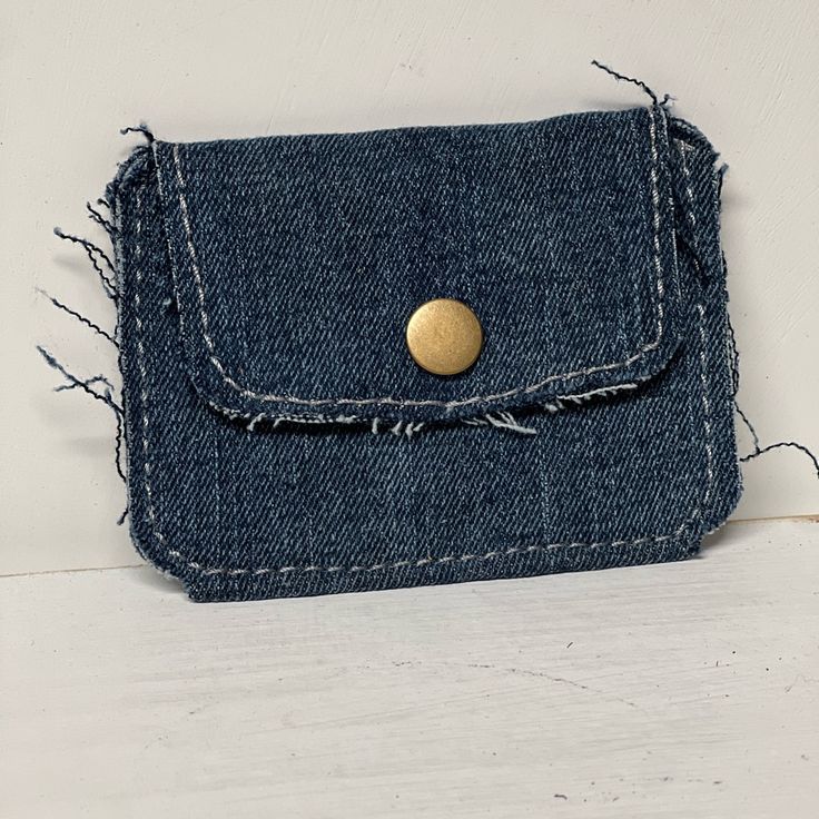 a denim purse with a gold button on the front and back flap, sitting on a white surface