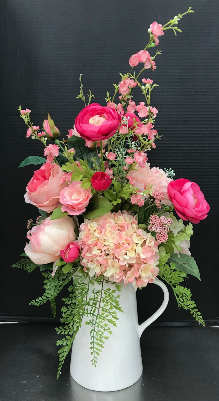 a white pitcher filled with pink flowers and greenery