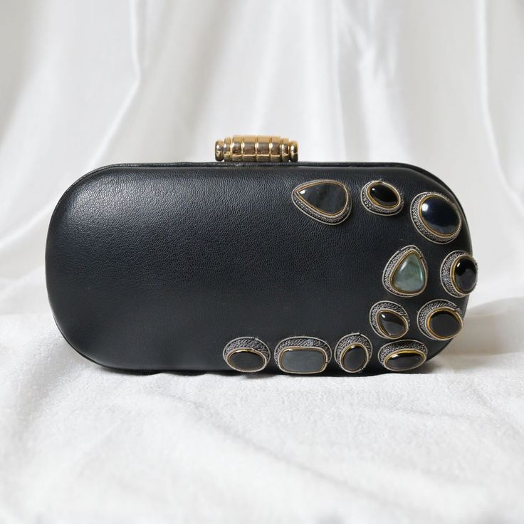 Hand-crafted with perfection, this luxury statement black leather clutch purse is exclusively embroidered with super-fine zardosi metallic thread. It's rarest combination of high-quality leather and zardosi metallic thread and genuine Onyx & Labradorite gemstones makes it opulent in its class. This comes under limited winter collection under the brand Zardouzee by Alark Lal. The metallic frame wrapped with leather looks awesome in parties and can also be carried easily in other formal events. With satin lining and pockets which can carry enough essentials like, mobile, small mirror, lipstick etc. Expertly hand embroidered by the most skilled zardozi artisans! Hand made in India! Size: 20*10*6 Utility: Shoulder Bag, Hand Clutch Bag Material: Leather, Metal Zari Stones: Onyx & Labradorite Ba Elegant Hand Embellished Black Bag, Elegant Black Hand-embellished Bag, Elegant Black Hand-embellished Clutch, Elegant Black Hand Embellished Clutch, Luxury Hand-embellished Black Evening Bag, Luxury Hand Embellished Black Evening Bag, Luxury Black Hand Embellished Evening Bag, Hand Embellished Black Evening Bag, Hand Embellished Black Evening Bag For Parties