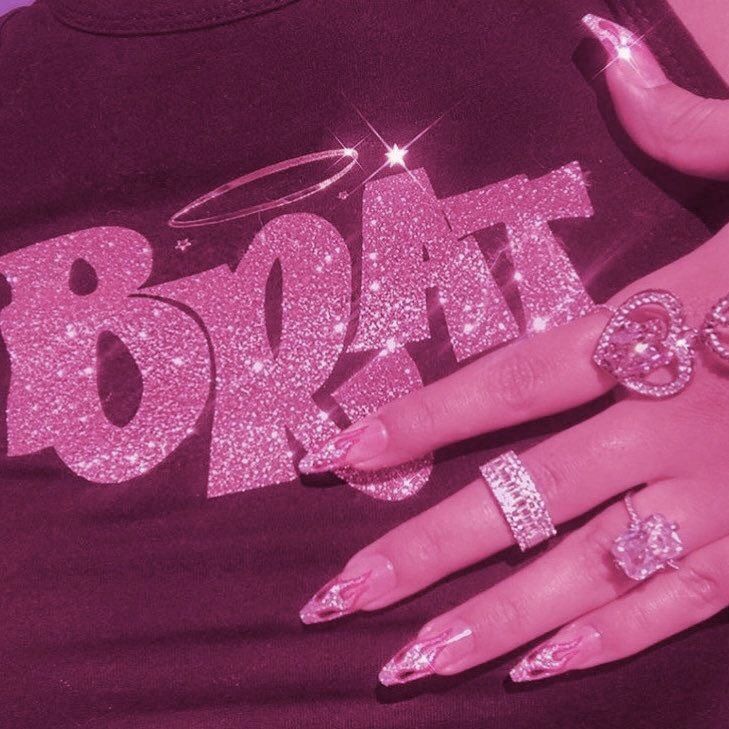 a woman with pink nails and rings on her hand, wearing a shirt that says brokatt