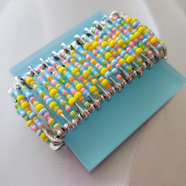 a colorful beaded bracelet sitting on top of a blue piece of paper with silver wire