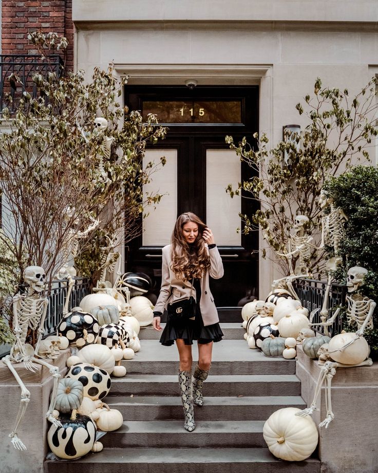 a woman standing on the steps in front of a building with pumpkins and skeletons