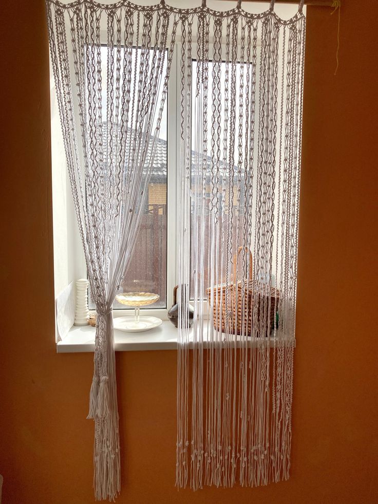 a window with sheer curtains and a basket on the windowsill in front of it