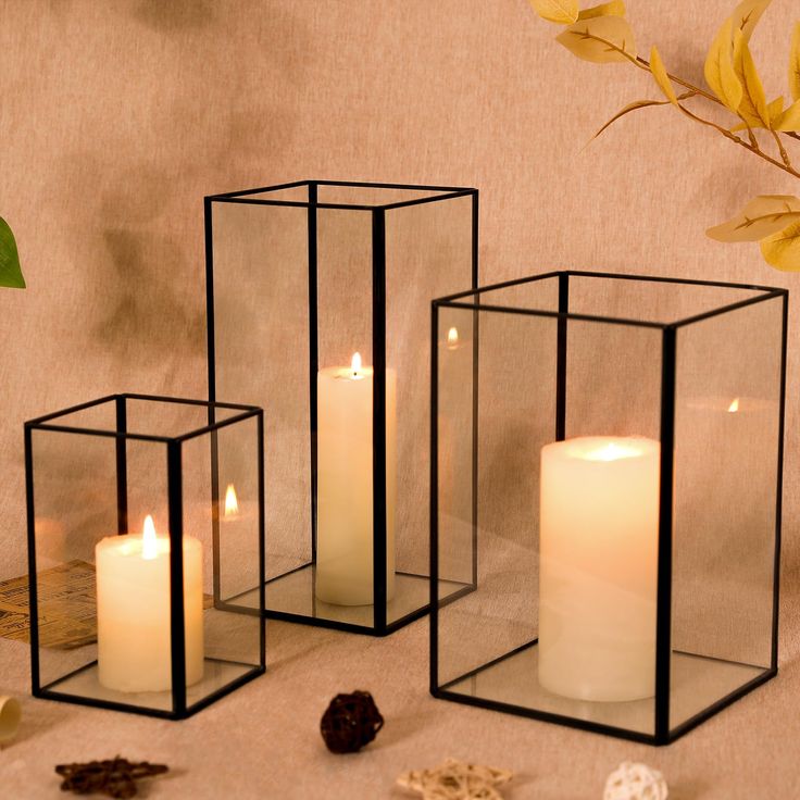 three glass cubes with lit candles on the floor next to some rocks and flowers