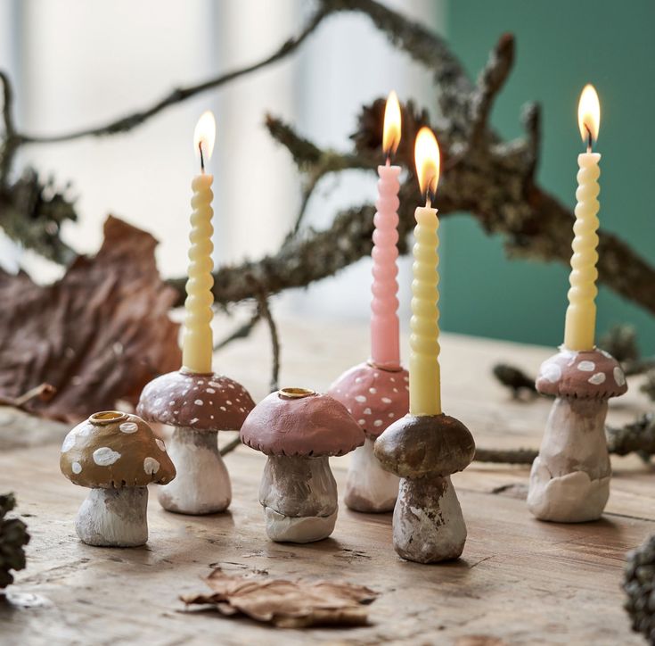 small mushrooms with lit candles in front of them on a wooden table next to leaves and acorns