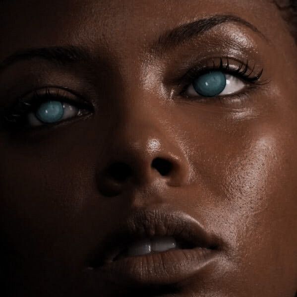 a woman's face with blue eyes and dark skin is shown in this image