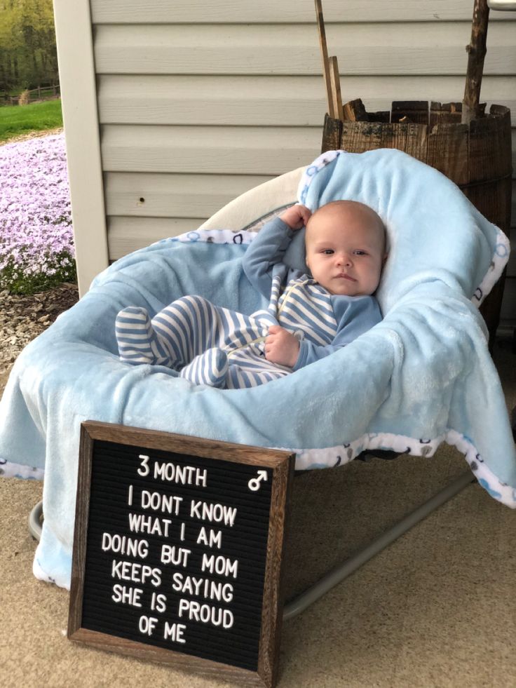 a baby laying in a blue blanket on top of a wooden chair next to a sign that says, 3 month i don't know what i am doing but mom keeps saying she s saying she is proud