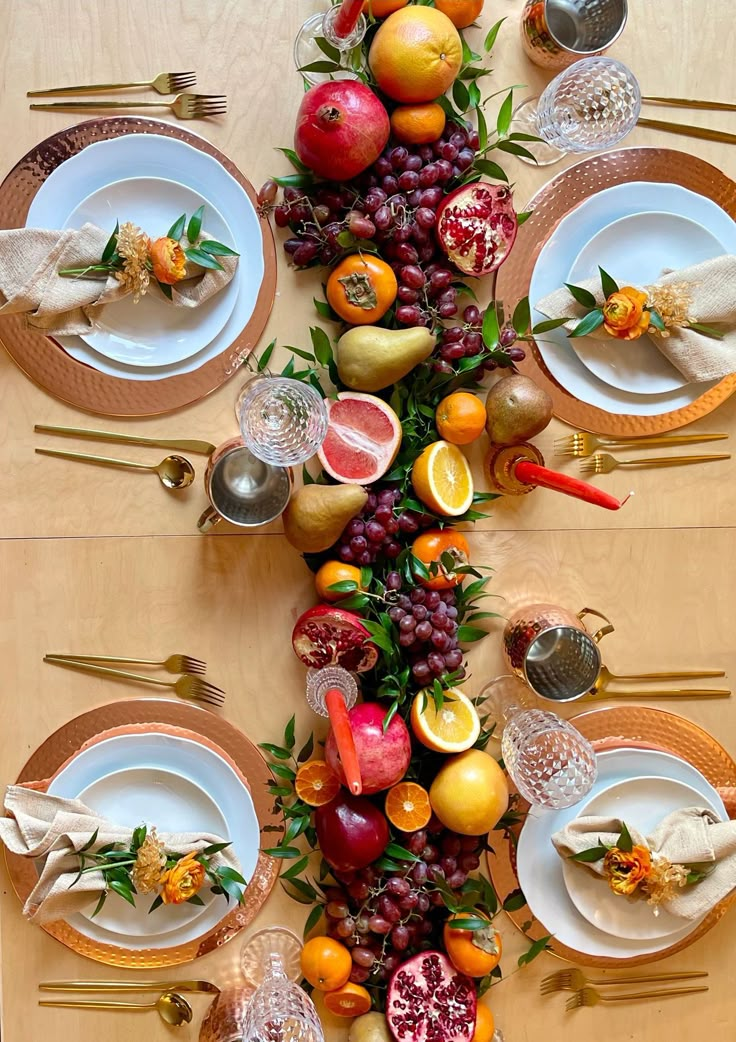 the table is set with plates, silverware, and fruit for a festive display