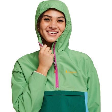 a woman wearing a green and blue jacket with a hoodie over her head, smiling at the camera