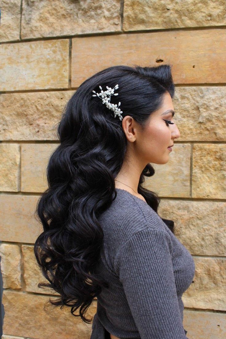 a woman standing next to a brick wall wearing a long black hair with flowers in her hair