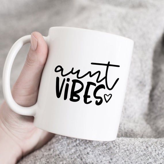 a person holding a white coffee mug with the words aunt vibes printed on it