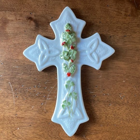 a ceramic cross with holly and red berries on it sitting on top of a wooden table