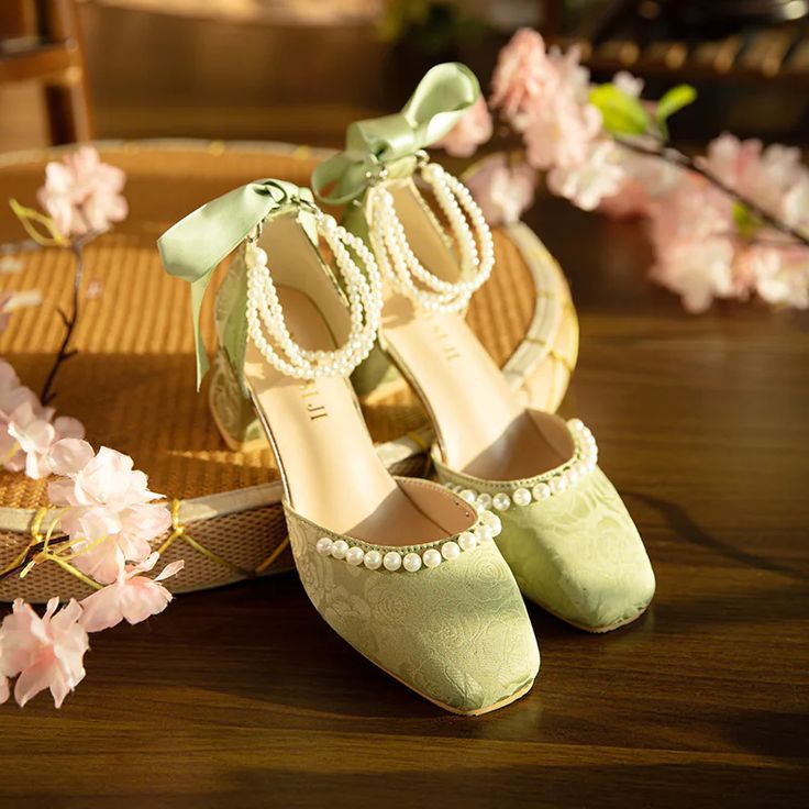 a pair of green shoes sitting on top of a wooden table next to pink flowers