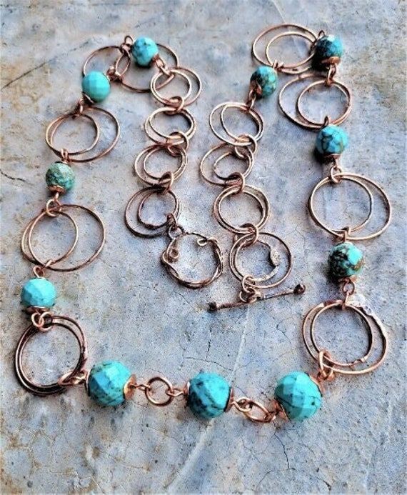 "Circles within circles in this gorgeous rustic Copper and genuine Turquoise necklace. Eight faceted 10mm genuine Turquoise rounds have hand-made Copper caps on top and bottom. These units are then formed as Copper links which connect to a cascade of big and bigger doubled-up hand-forged and soldered Copper wire rings. Three 12mm Copper capped Turquoise rounds are linked together and form the focal center of this lovely metallic draping necklace. This finishes with a hand-forged Copper toggle cl Rustic Jewelry With Natural Stones For Jewelry Making, Rustic Natural Stones For Jewelry Making, Turquoise Wire Wrapped Round Jewelry, Bohemian Hand Forged Round Jewelry, Turquoise Wire Wrapped Round Necklace, Artisan Round Turquoise Necklace For Jewelry Making, Artisan Handmade Circular Jewelry, Handmade Artisan Circle Jewelry, Adjustable Hammered Turquoise Jewelry