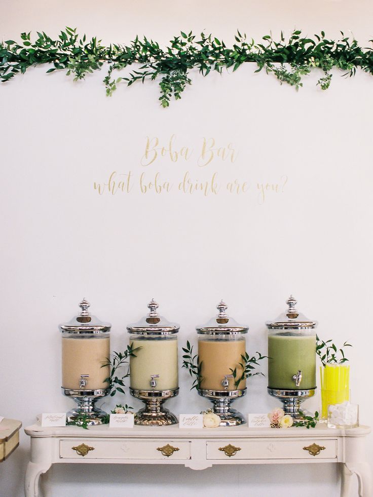 a table topped with three candles next to a wall covered in green leaves and greenery