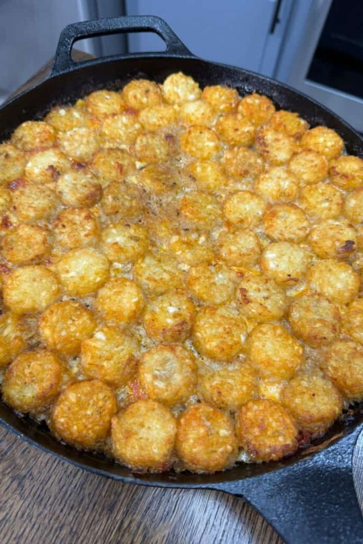 a skillet filled with tater tots sitting on top of a wooden table