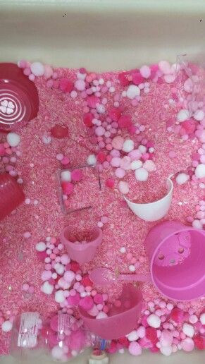 a bath tub filled with lots of pink and white bubbles next to bowls and cups