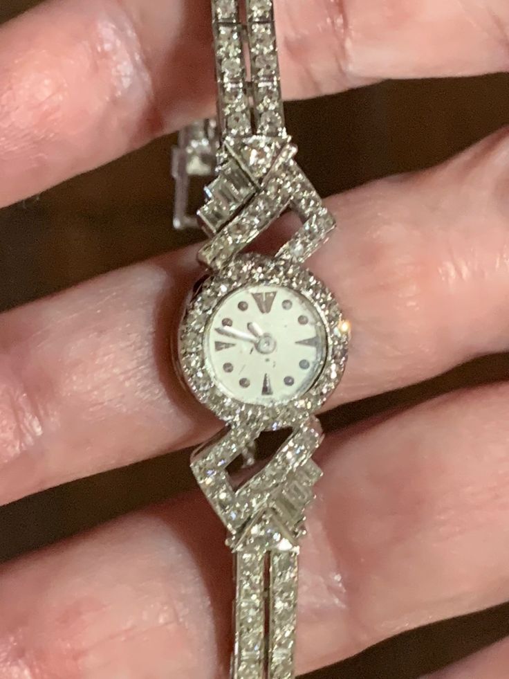 This stunning piece of fine jewelry is a vintage platinum and diamond Le Coultre lady's watch. There are 22 round single cut diamonds set around the case, each .01 ct. The case connector has 12 round single cut diamonds, 11 @ .02, 1 @ .04, and 3 straight baguettes, 1 @ .02, 1 @ .03, and 1 @ .05 cts. This identical pattern of diamonds repeats on the other side of the case. The band consists of 11 links that hold 4 @ .02 ct. single cut diamonds per link, 1 link of 3 straight baguettes diamonds @ 0 Classic Diamond White Watch With Brilliant Cut, Classic Diamond White Round Diamond Watch, Classic Diamond Jewelry With Brilliant Cut, Classic Round Diamond Watch For Formal Occasions, Classic Diamond Watch For Formal Occasions, Diamond Watch With Brilliant Cut, Classic Diamond White Watch For Anniversary, Timeless Diamond Watch With Diamond Hour Markers, Timeless Round Diamond Watch With Diamond Hour Markers