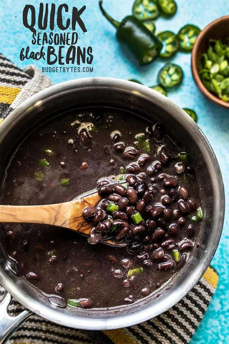 black beans are being cooked in a pot with a wooden spoon and green peppers on the side