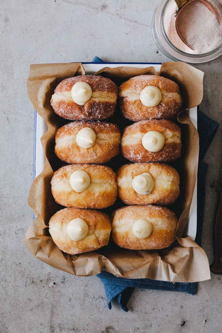 a box filled with donuts next to a cup of powdered sugar on top of a table