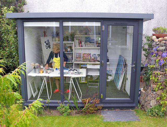 a woman sitting at a table in front of a garden shed